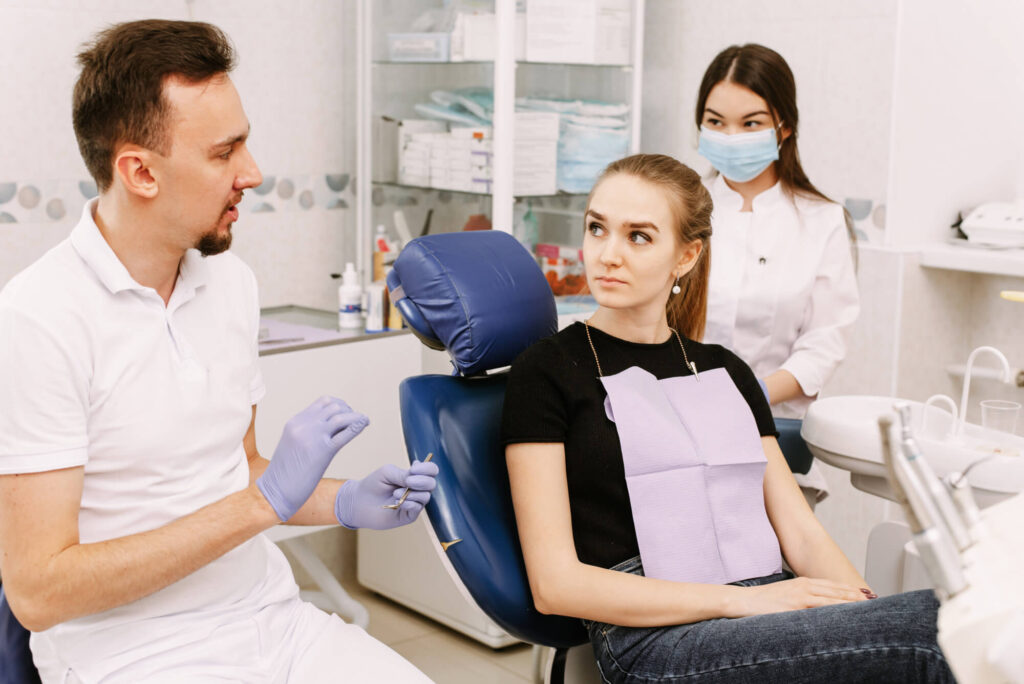 Dentistry. The dentist and his assistant are talking to the patient. The patient is sitting in a chair.